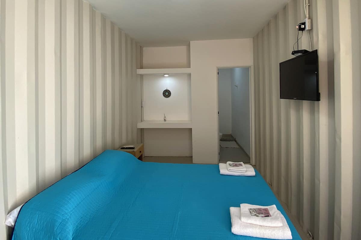 A hotel room with a single bed, a TV mounted on the wall, and a small desk with a chair.