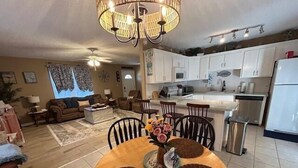 A modern kitchen with white cabinets, a stainless steel refrigerator, and a dining area with a wooden table and chairs.