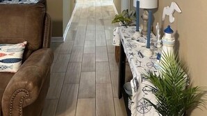 A hallway with a brown leather couch, a table with a nautical-themed tablecloth, and various wall decorations including a seahorse and a ship painting.