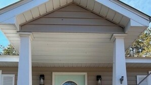 A house with a light blue door, white columns, and a covered porch with steps leading to the entrance.