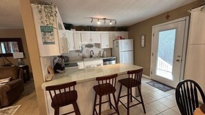 A kitchen with white cabinets, a central island with stools, a refrigerator, and a sink.