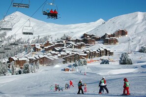 Ein Skigebiet mit mehreren Chalet-ähnlichen Gebäuden, Skiliften und verschneiter Landschaft.