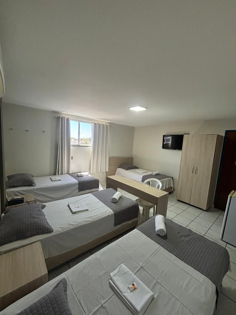 A hotel room with two single beds, a desk, a chair, a TV, and a wardrobe.