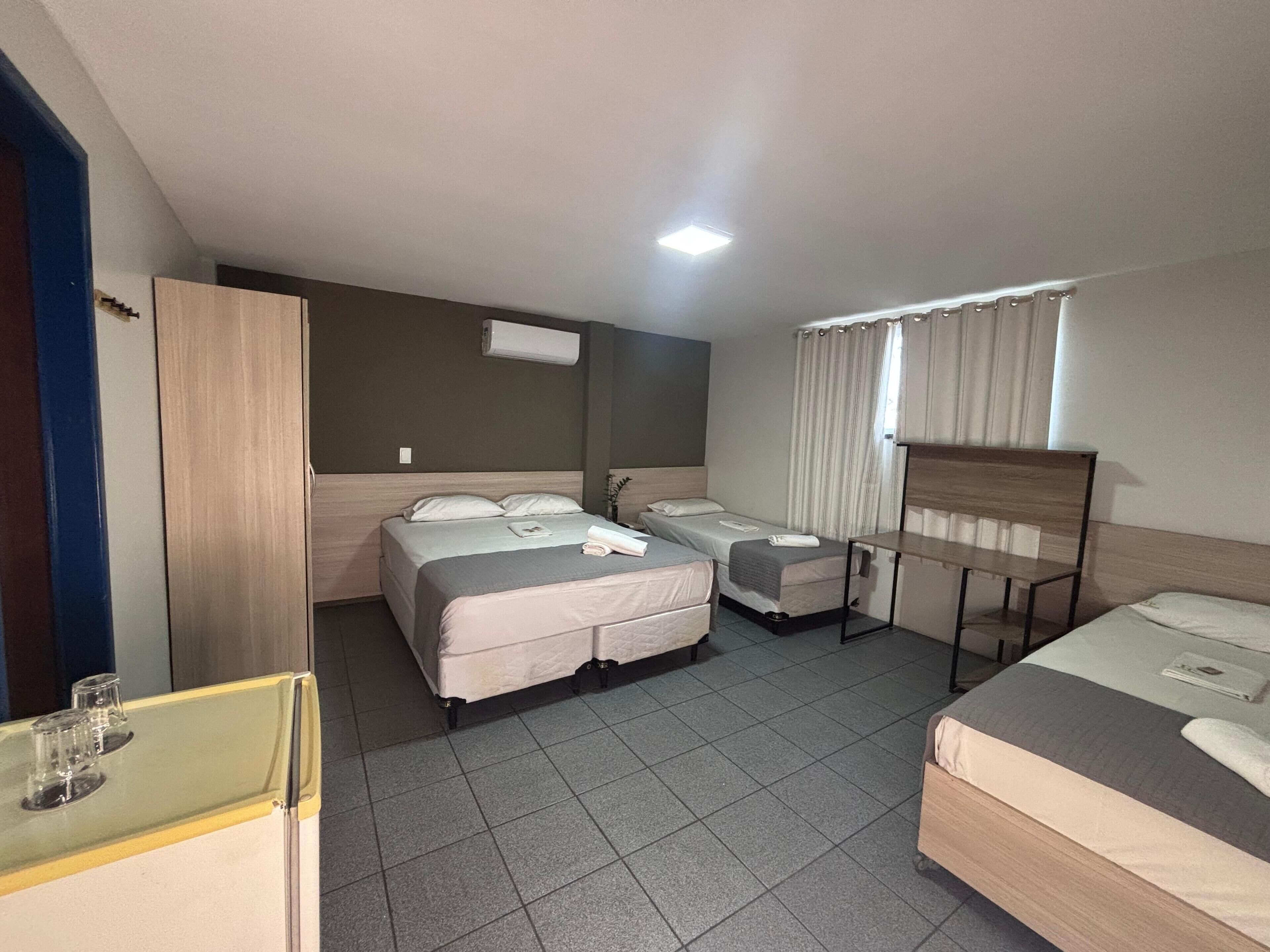 A hotel room with two beds, a desk, a wardrobe, and a window with curtains.