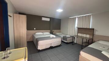 A hotel room with two beds, a desk, a wardrobe, and a window with curtains.