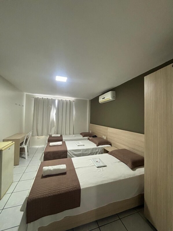 A hotel room with two beds, a desk, a chair, a window with curtains, and an air conditioning unit. - Executivo Prime Hotel (Teresina)