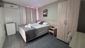Una habitación de hotel con cama, mesita de noche, armario y dispensador de agua.
