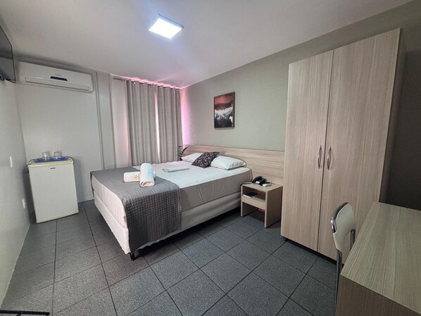 A hotel room with a bed, bedside table, wardrobe, and a water dispenser. - Executivo Prime Hotel (Teresina)