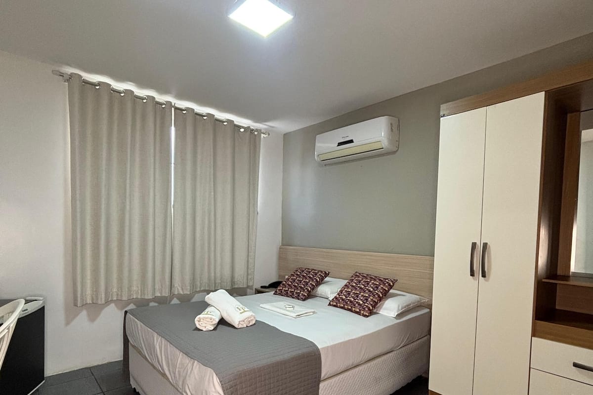 A hotel room with a bed, a wardrobe, an air conditioning unit, and a curtain.