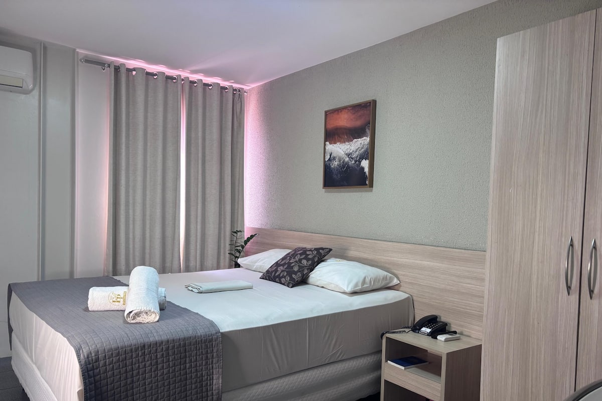 A hotel room with a bed, a nightstand, a wardrobe, and a painting on the wall.