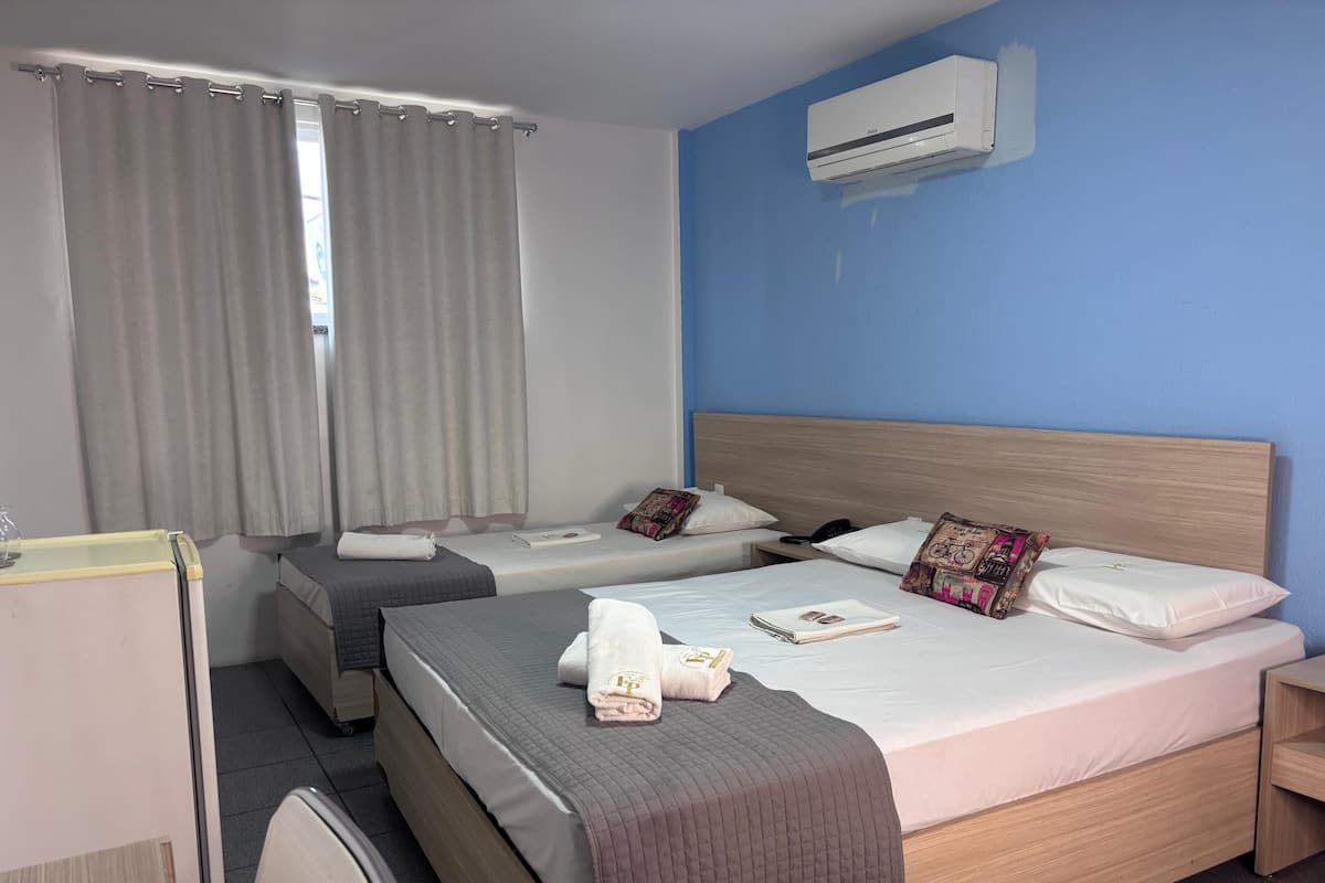 A hotel room with two beds, a desk, a chair, an air conditioning unit, and a window with curtains.