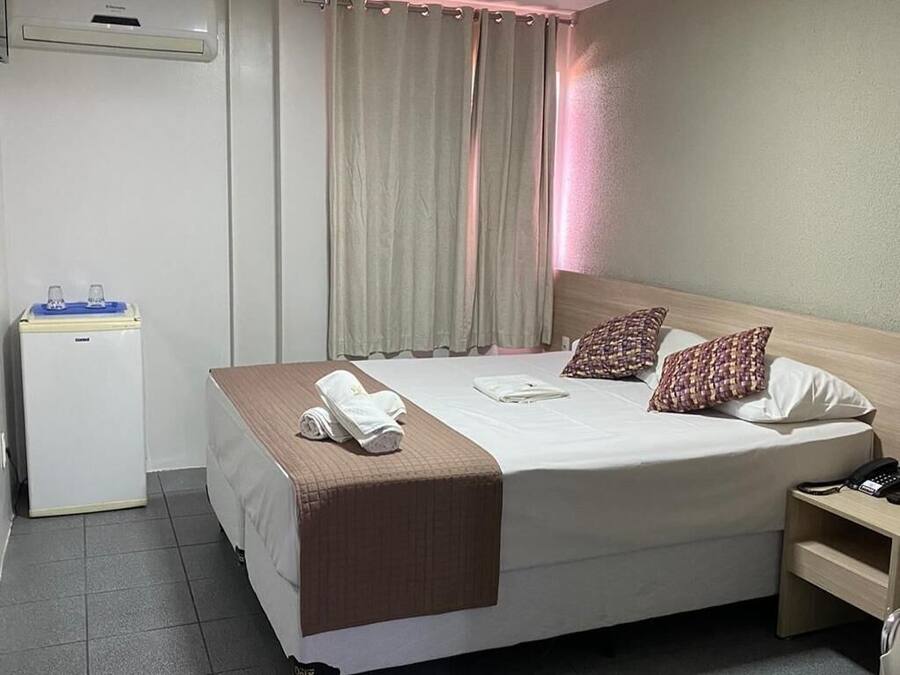 A hotel room with a bed, bedside table, lamp, and a small desk with a chair.