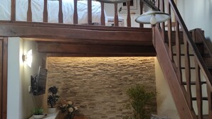 Una stanza in stile loft con una scala in legno, un muro in pietra, un divano bianco e un piccolo armadietto bianco.