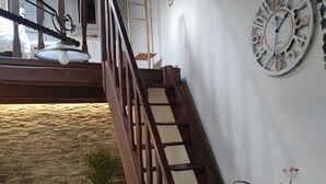 Una scala con ringhiere in legno conduce a un piano superiore, con a fianco un muro in pietra, un divano bianco e un orologio a parete.