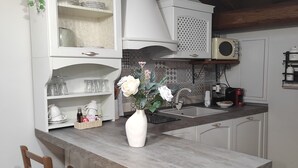 Una cucina con isola centrale, due sedie di legno, un vaso bianco con fiori e un forno a microonde sopra il lavello.