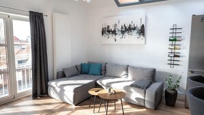 A modern living room with a grey sectional sofa, a small wooden table, and a cityscape painting on the wall. - Zentral am Stadtwald (Hannover)