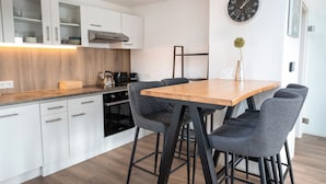 A modern kitchen with white cabinets, a wooden countertop, a black stove, and a dining area with a wooden table and grey upholstered chairs. - Zentral am Stadtwald (Hannover)