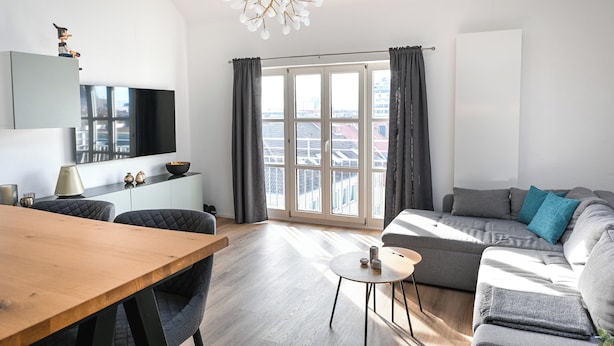 A modern living room with a wooden dining table, grey sofa, and a large window with curtains. - Zentral am Stadtwald (Hannover)