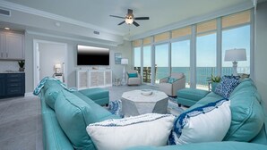 Un salon spacieux avec des canapés de couleur turquoise, une table basse ronde et un ventilateur de plafond.
