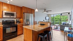 A modern kitchen with wooden cabinets, a stainless steel microwave, a black stove, and a large island with stools.