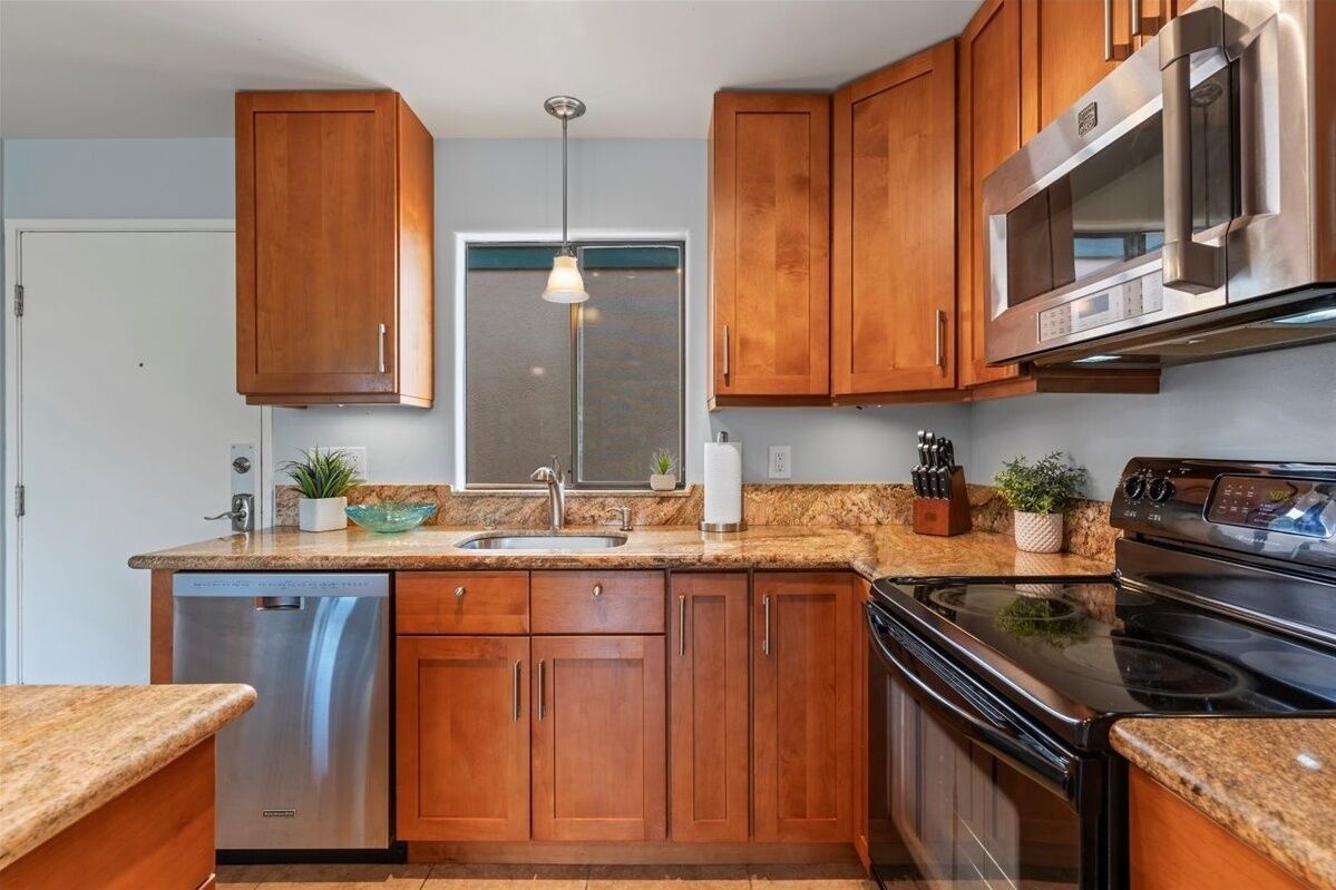 A kitchen with wooden cabinets, a stainless steel dishwasher, a built-in oven, and a microwave.