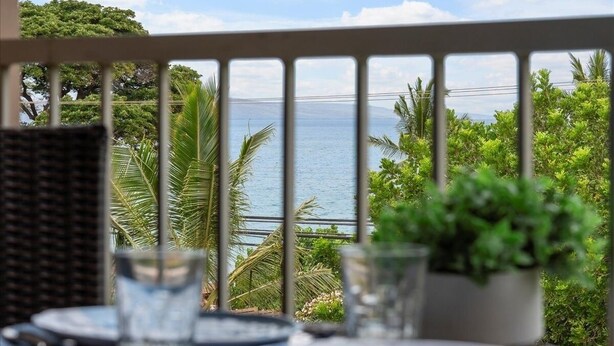 A balcony with a view of the sea, a wicker chair, and a table with plates and glasses.