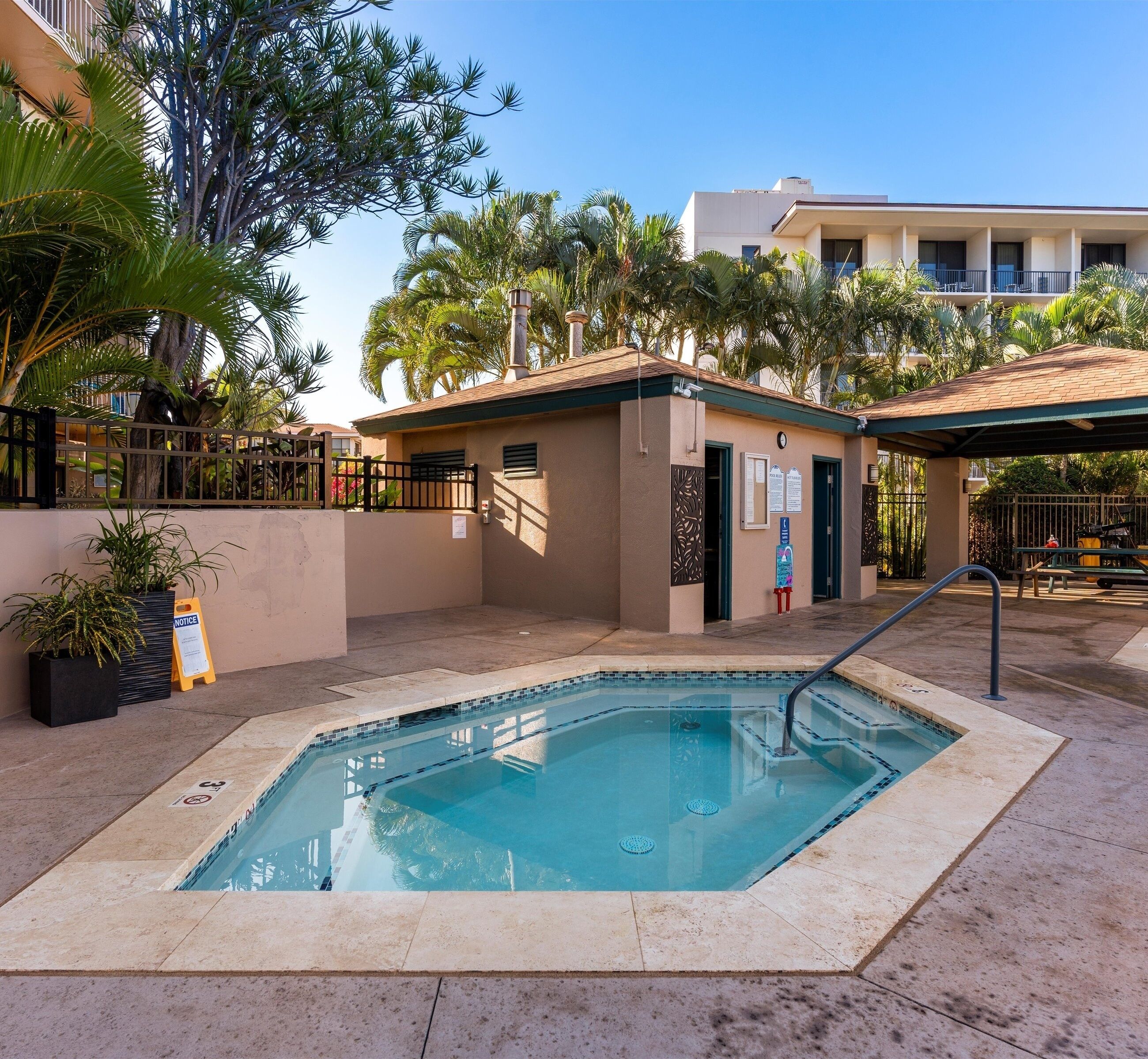 A swimming pool with a tiled deck, surrounded by palm trees and a building with a beige facade.