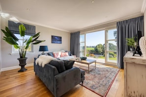 A spacious living room with a large window, a sofa, a coffee table, and a potted plant.