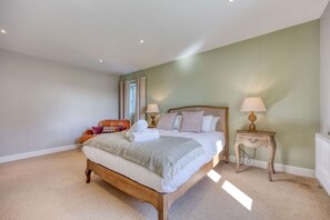 A bedroom with a large bed, two bedside tables with lamps, a chair, and a window with curtains.
