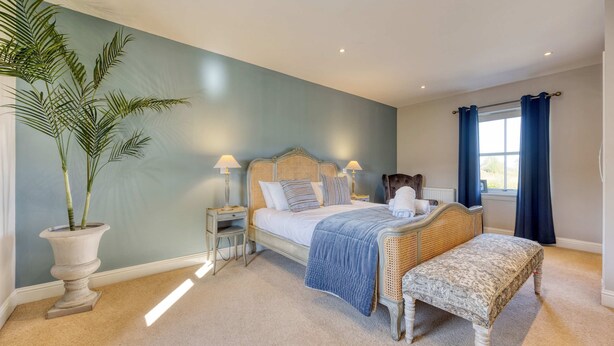 A bedroom with a bed, bedside tables, a bench, a potted plant, and a window with curtains. - Farmhouse Retreat with Large Hot Tub (Bishopton)