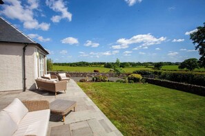 A patio with wicker furniture and a stone pathway leading to a grassy lawn.