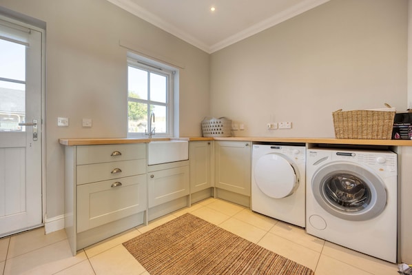 A laundry room with a washing machine, a dryer, a window, and a small basket on the countertop.