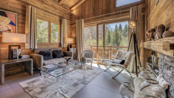 A cozy log cabin interior with a sofa, armchairs, a glass coffee table, and a fireplace. - Chalet apartment in Megève (Megève)