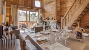 A wooden interior with a dining area set for four, a fireplace, and a view of the outdoors. - Chalet apartment in Megève (Megève)