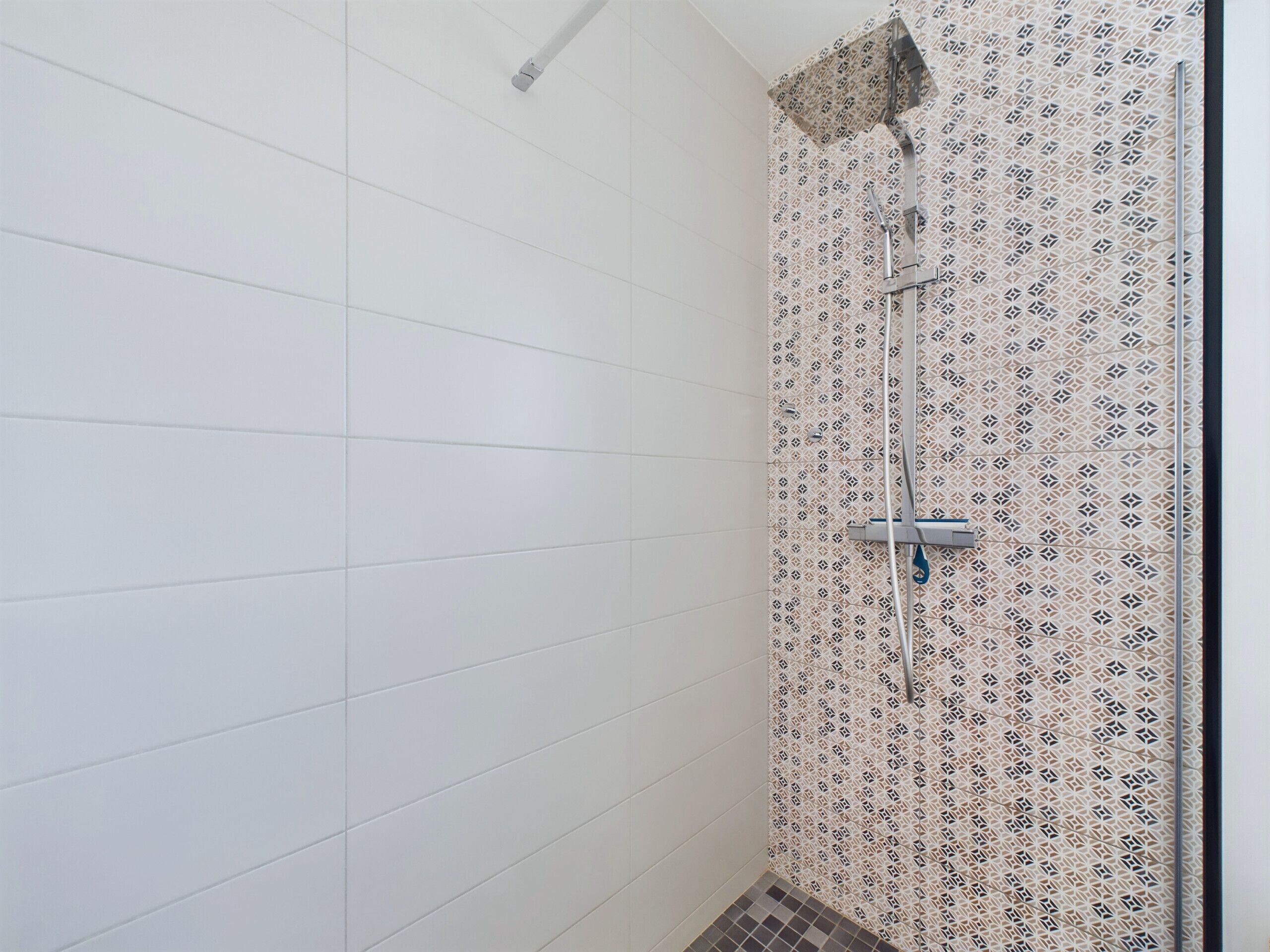 Eine Dusche mit einer Wand mit Muster und einem Fliesenboden.