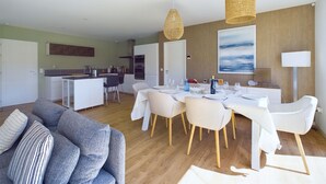 A modern living room with a grey sofa, dining table set for six, and a kitchen in the background. - House for 7 with a pool (6 adults maximum) (Saint-Hilaire-de-Riez)