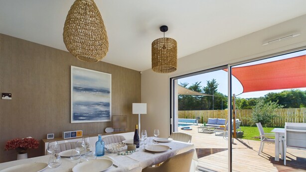 A dining area with a table set for four, a large painting on the wall, and a view of the outdoor deck and pool. - House for 7 with a pool (6 adults maximum) (Saint-Hilaire-de-Riez)