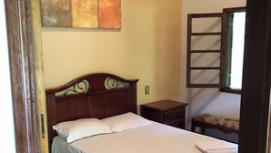 Ein Schlafzimmer mit einem hölzernen Bett, einem Nachttisch, einer Bank und einem Fenster.