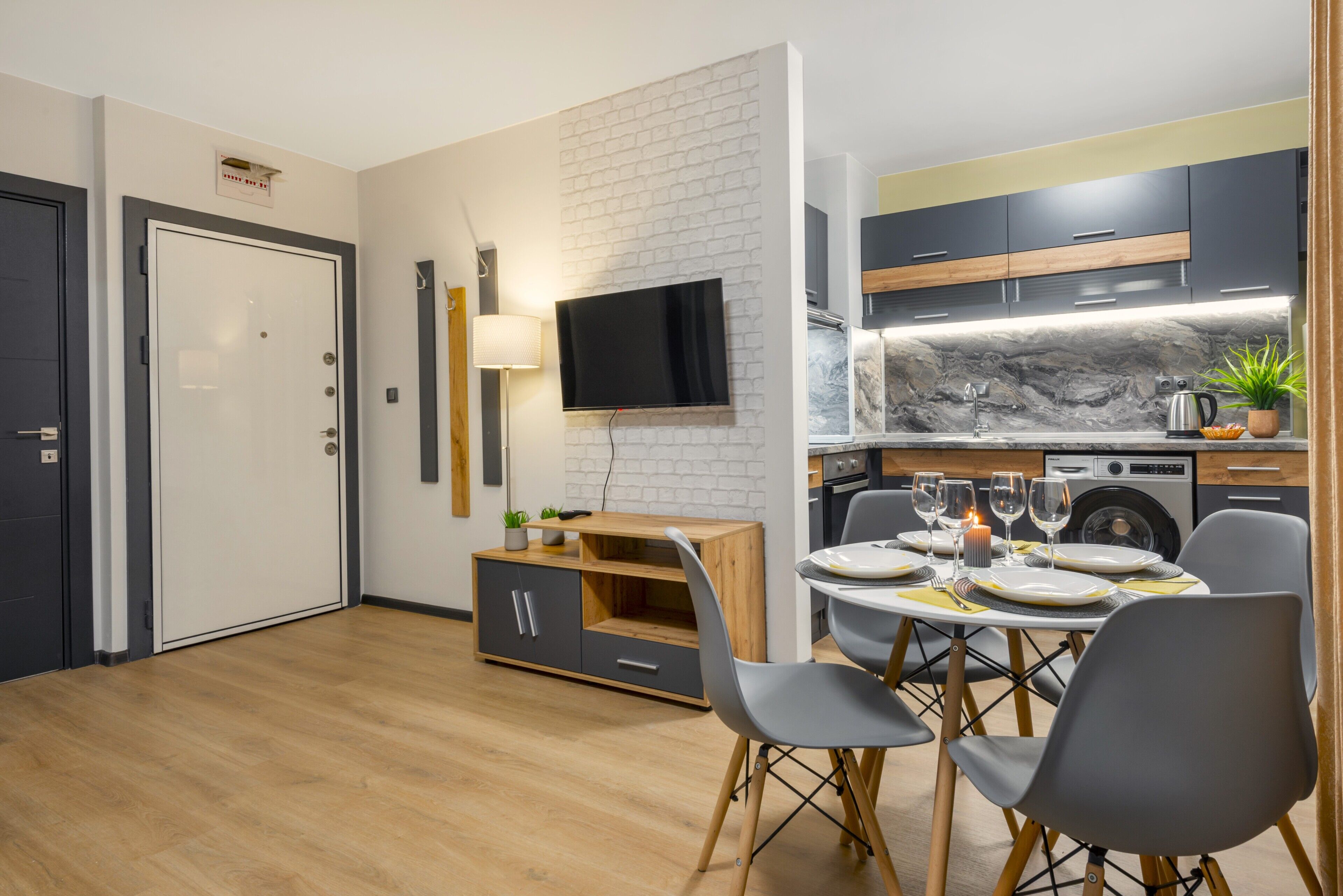Una cocina moderna con salpicadero de mármol, una zona de comedor con sillas grises y un televisor de pantalla plana montado en la pared.