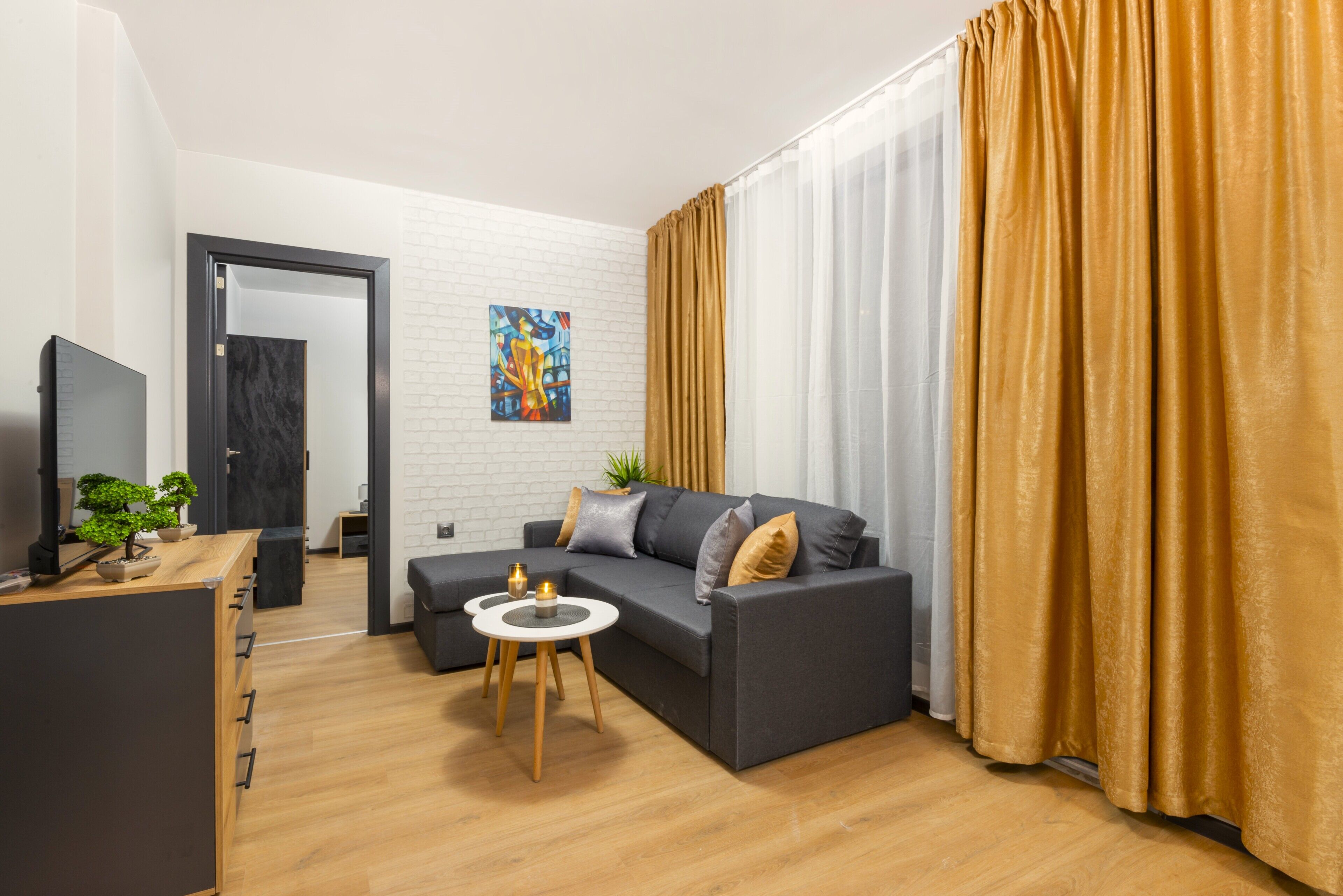 A modern living room with a grey sofa, a small round table, a TV, and a plant.