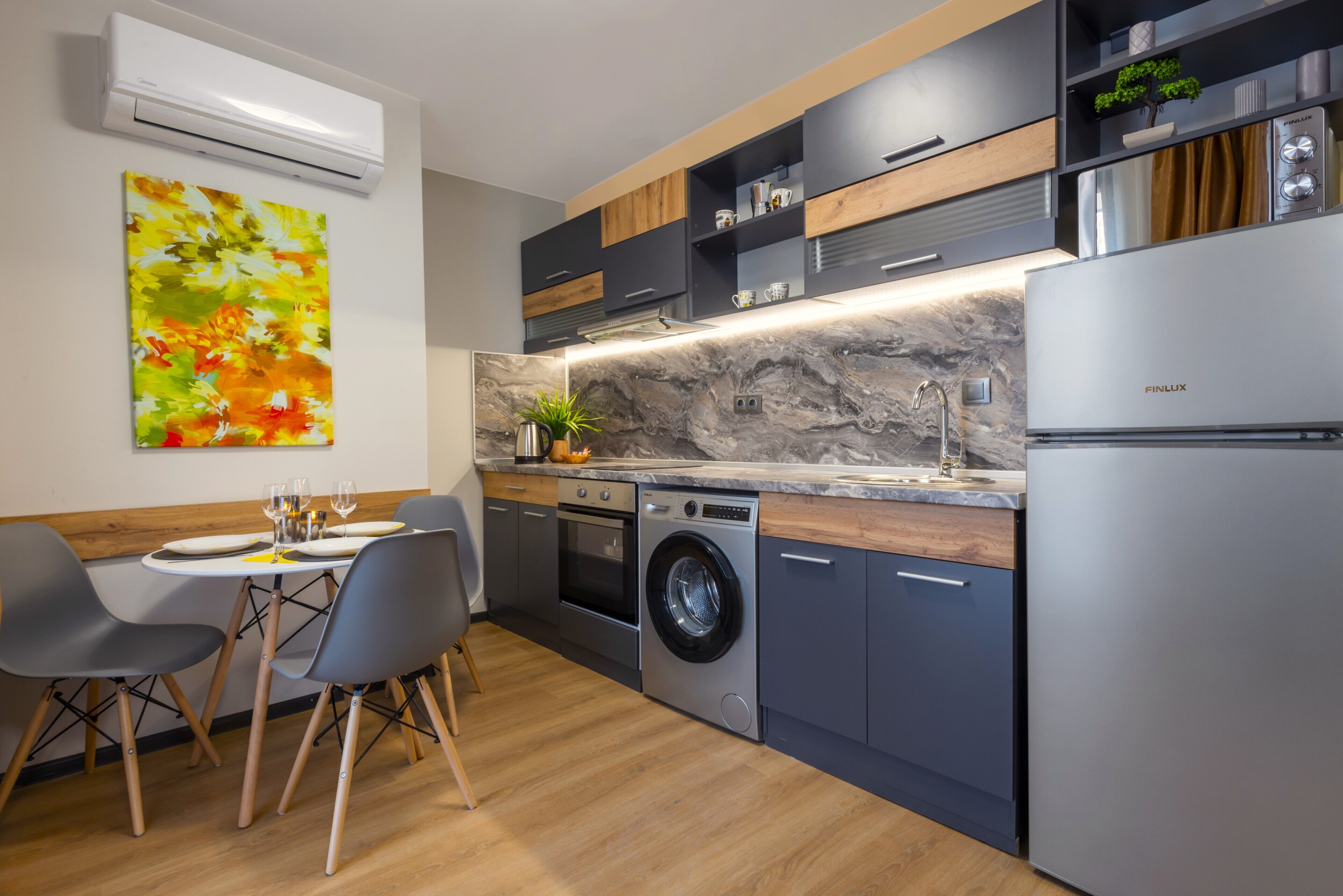 A modern kitchen with a built-in washing machine, a dining area with chairs, and a large air conditioning unit on the wall.