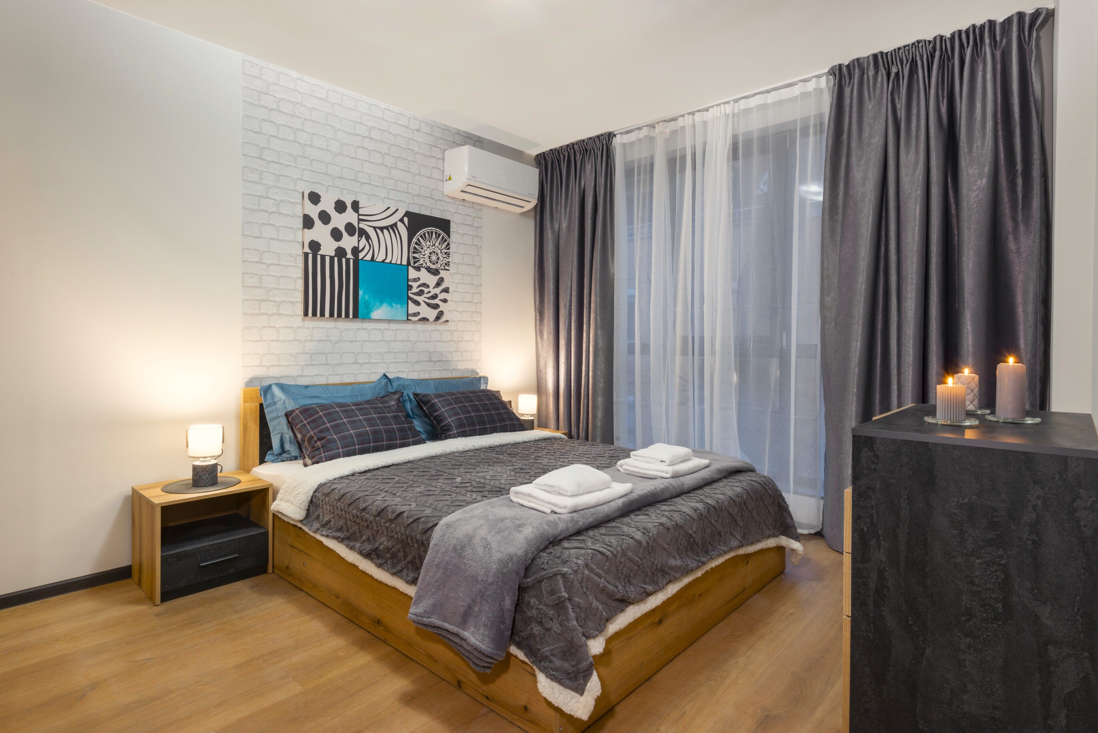 Een moderne slaapkamer met een houten bed, een nachtkastje, een wandairconditioner en een raam met dunne gordijnen.