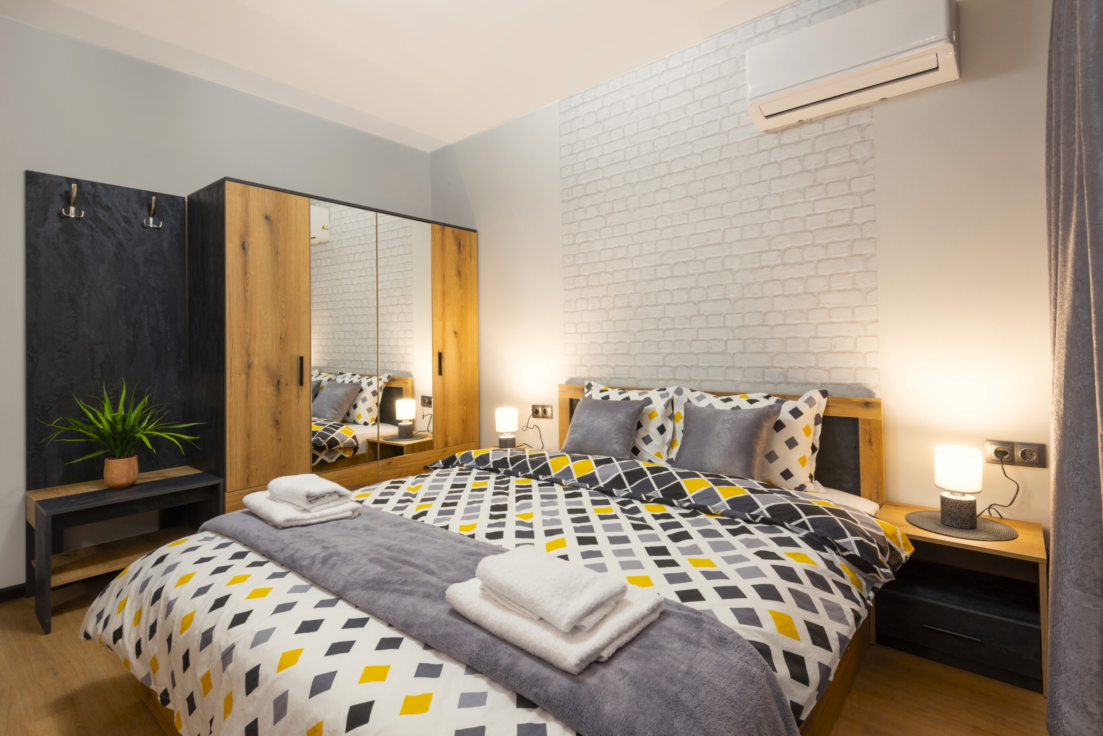 A modern bedroom with a large bed, a wardrobe, a bedside table with a lamp, and a potted plant.