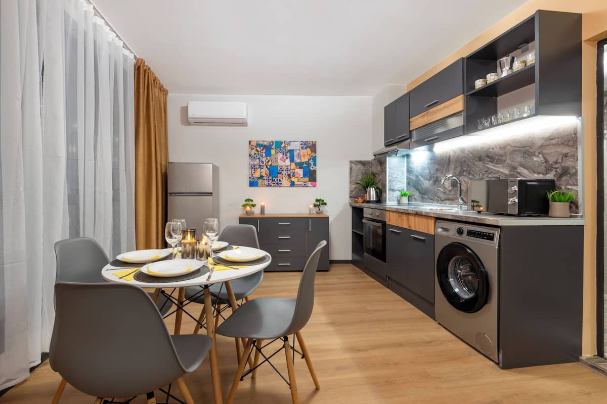 A modern kitchen with a built-in washing machine, a dining area with a table set for four, and a decorative wall piece.