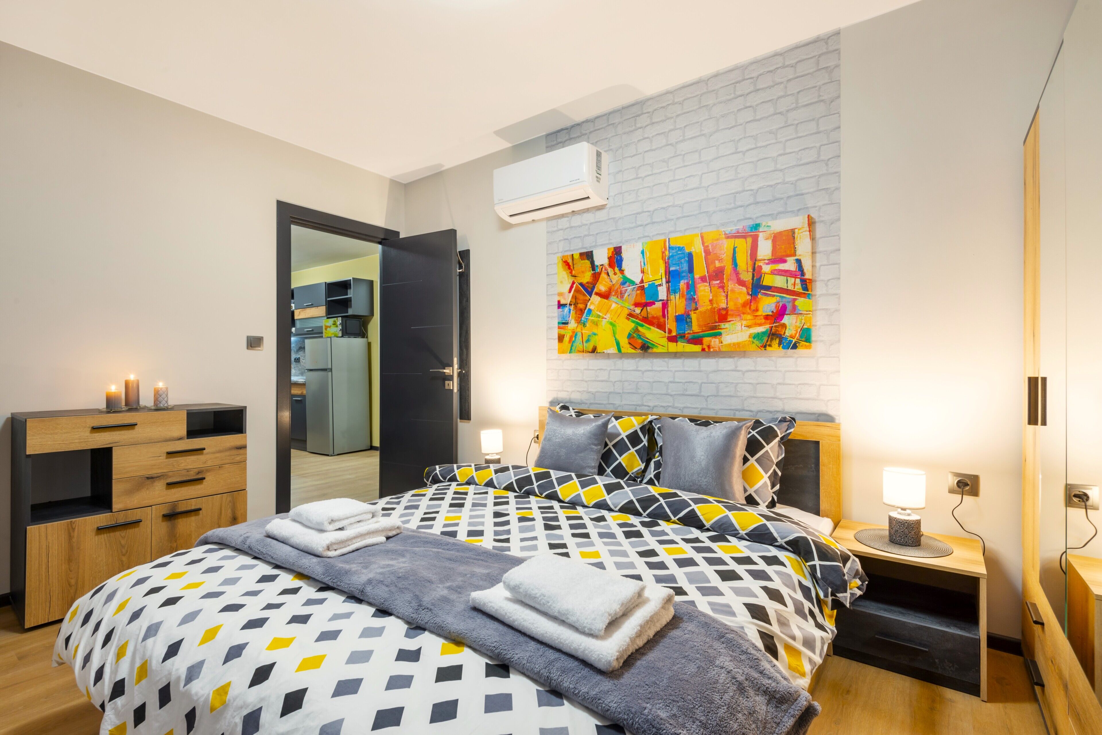 A modern bedroom with a bed, bedside tables, a dresser, and a colorful abstract painting on the wall.