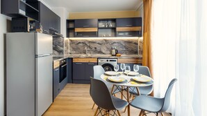 A modern kitchen with dark cabinets, a marble countertop, and a dining area with a table set for four. - Best Guest 2 Apartments (Plovdiv)