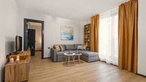 A modern living room with a grey sofa, wooden coffee table, and a white brick wall. - Best Guest 2 Apartments (Plovdiv)