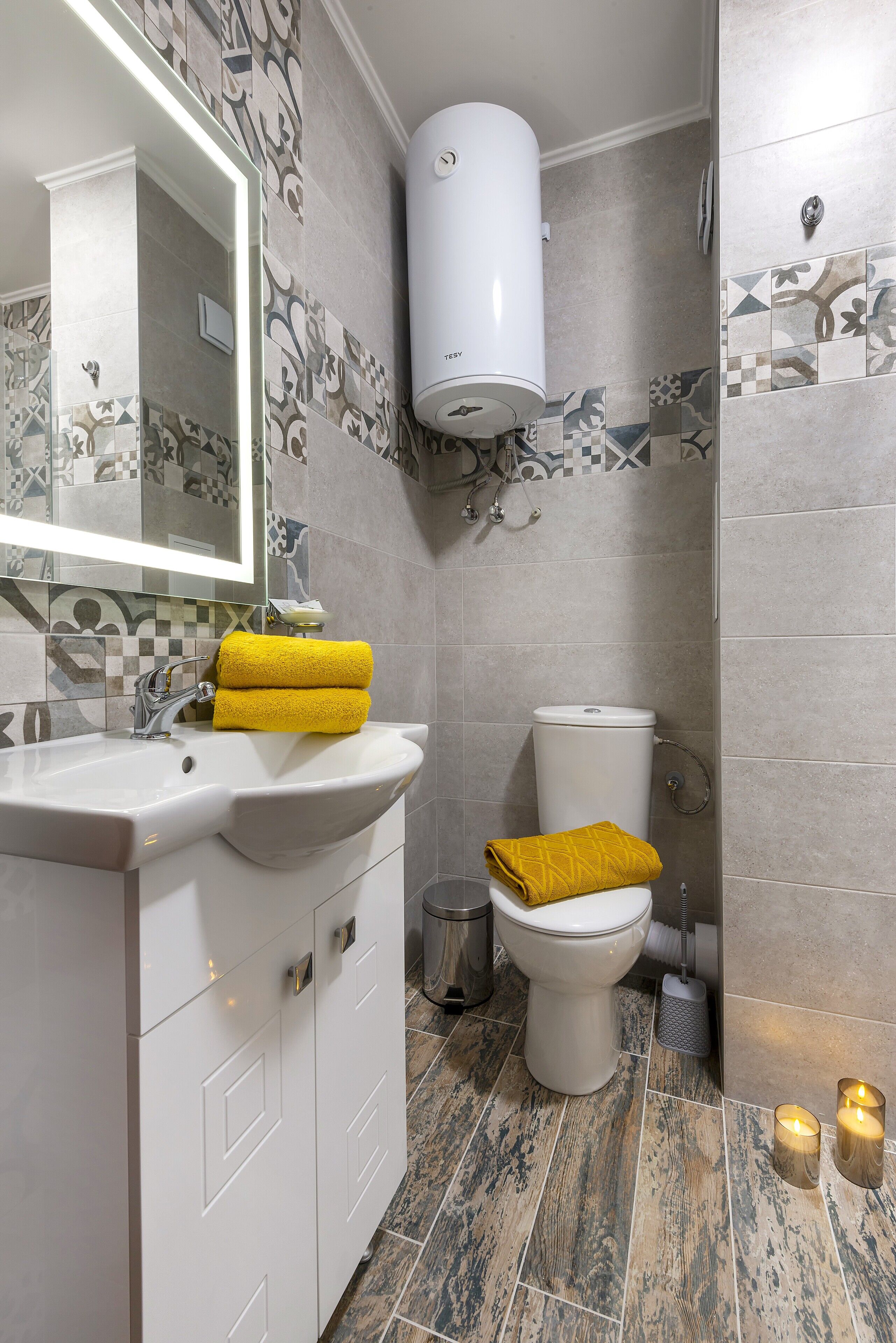 Un baño con un lavabo blanco, un inodoro y un espejo. Hay dos toallas amarillas sobre el lavabo y el inodoro.