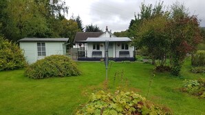 A house with a front yard, a small shed, and a garden with various plants.