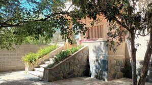 Un escalier en pierre mène à un balcon orné de plantes en pot, d’où l’on peut admirer un immeuble dont une fenêtre est munie de barreaux.